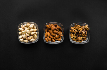 Almond, pistachio and walnut in a small plates which standing on a black table. Nuts is a healthy vegetarian protein and nutritious food.