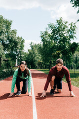 Naklejka premium Young couple in starting position on running track in park