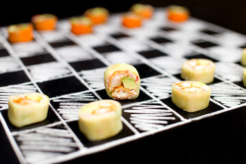 Playing chess with Japanese sushi roll pieces without rice on chalkboard background. Healthy sushi with cucumber instead rice on drawn chessboard. Asian sushi with crunchy shrimp and avocado
