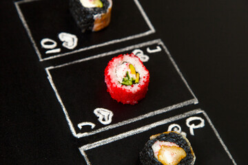 Poker cards with Japanese sushi roll pieces on dark chalkboard background. Asian roll with flying fish roe, cucumber and avocado in focus near black rice rolls. Ten, Jack and Queen of Hearts cards
