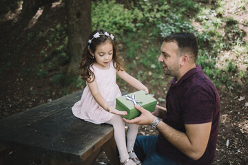 Daughter giving present to his father in forest. Smiling man squatting in nature while holding gift...