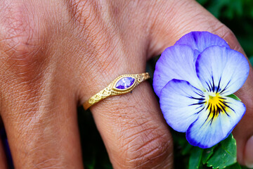 Hand wearing metal decorative ornamental ring with amethyst gemstone, touching plants