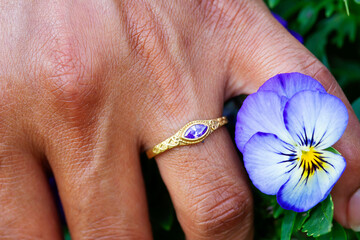 Hand wearing metal decorative ornamental ring with amethyst gemstone, touching plants
