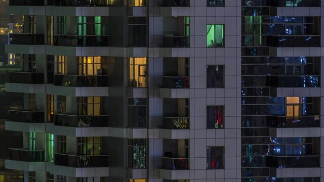 Rows of glowing windows with people in the interior of apartment building at night. Modern skyscraper from glass and concrete. Concept for business and modern life. Tilt down