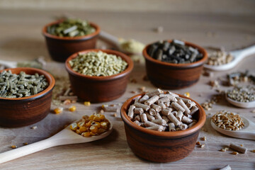 Different kinds of pelleted compound feed in bowls and spoons on wood table, copy space