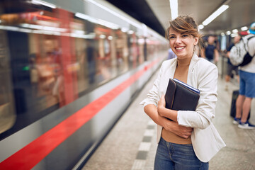 young business woman at subway station holding folder and notebook with hands crossed, smiling. Body language. Time concept