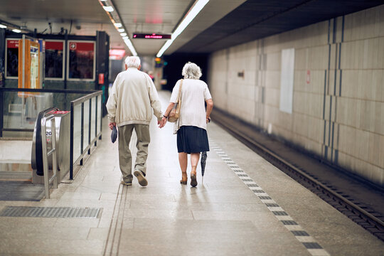 elderly couple holding hands in subway, walking