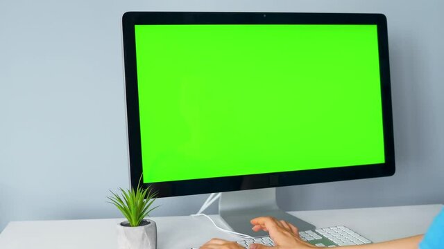 Woman typing on a computer keyboard, monitor with a green screen. Chroma key. Copy Space.