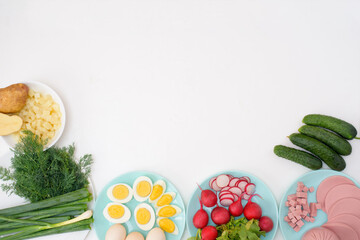 ingredients for a recipe of homemade Russian national cold okroshka soup on a light background. potatoes, radishes, sausage, onions, herbs, eggs. the view from the top