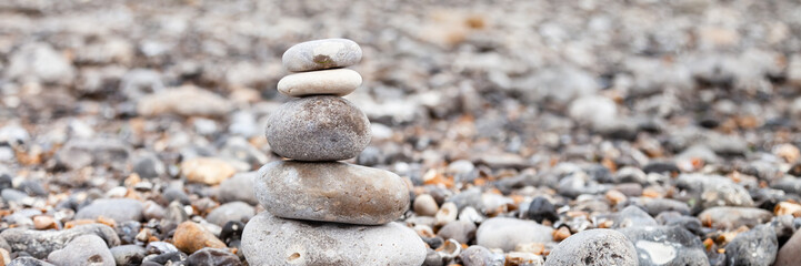 Grey pebble stones pyramid on the beach. Concept of zen, stability, harmony, balance. Close up, macro. front view. Blue ocean water on the background. North of France, Normandy. Banner