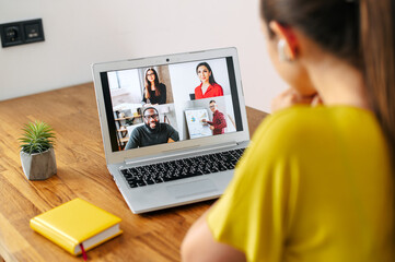 Virtual conference, online meeting. Young woman uses laptop app for communicating with several people friends or employees at same time together. Back view. Video call concept