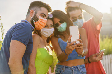 Happy Friends with protective safety mask having fun making selfies during coronavirus (COVID-19) pandemic in the summer.