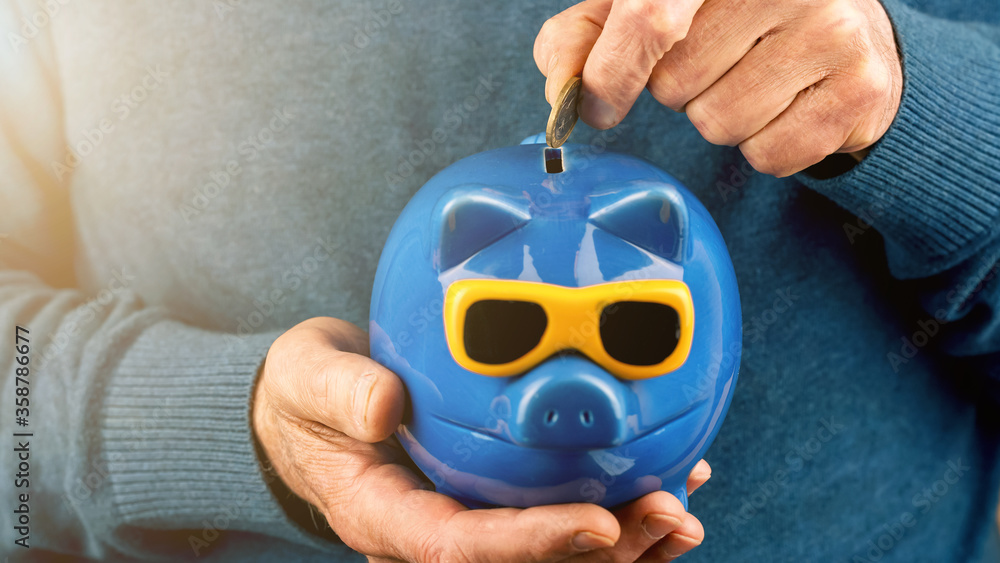 Wall mural pensioner puts coin into blue piggy bank slot closeup