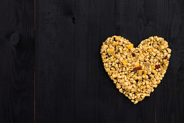 Heart laid out of granola on black wooden background. Flat lay. Copy space.