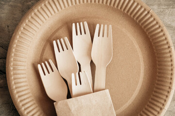 Wooden forks and plates on wooden background. Eco friendly disposable tableware. Also used in fast food, restaurants, takeaways, picnics. Top view. Copy, empty space for text