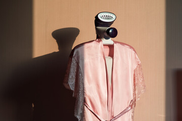 Pnk silk robe hanging on vertical iron steamer. Pink background. Bedroom .