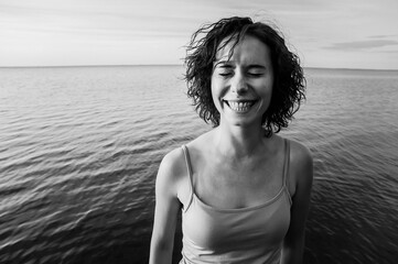 a girl smiling wide with closed eyes with a sea on the background