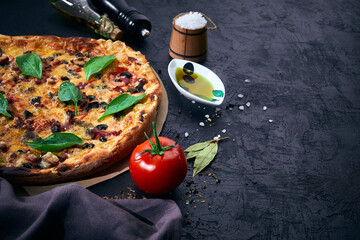 Italian pizza and pizza cooking ingredients on dark background. Tomatoes, olives oil, herbs, salt...
