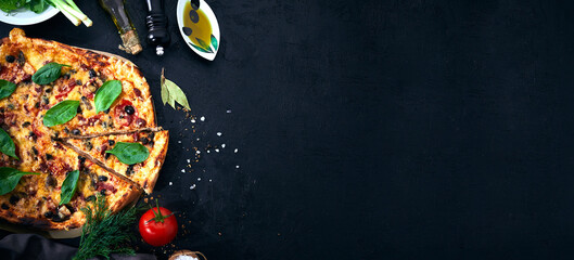 Italian pizza and pizza cooking ingredients on dark background. Tomatoes, olives oil, herbs, salt and spices. Banner view.