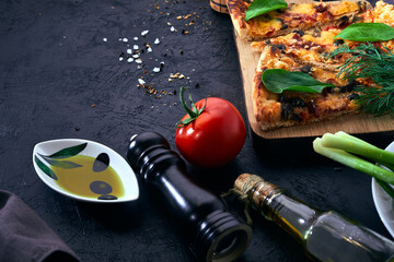 Italian pizza and pizza cooking ingredients on dark background. Tomatoes, olives oil, herbs, salt...