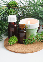 Small glass bottles with essential pine oil and burning candle. Pine branches and cone close up. Aromatherapy, spa and herbal medicine ingredients. Copy space.