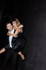 Smiling woman in bunny ears piggybacking on man in suit on black background