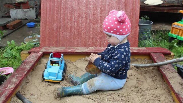 Focused preschool girl in casual wear, playing alone sand and toy supplies in a sandbox in the countryside. Baby looks up at the sky and sighs