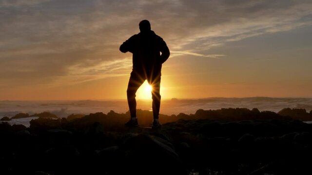 Young men warrior monk practicing silhouette tai chi karate kung Fu on the rocky stones horizon at sunset or sunrise. Silhouette on a background of dramatic epic waves at pacific coast