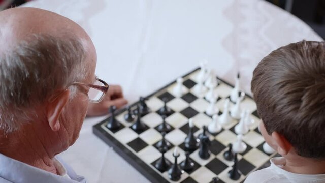 educational games, a little smart boy plays board games of chess with his caring grandfather sitting at a table during a family vacation