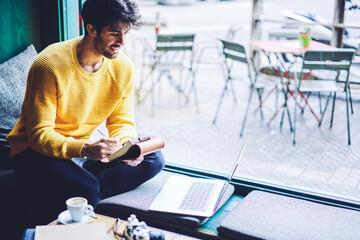 Cheerful male international student in casual outfit sitting in coffee shop preparing homework task...