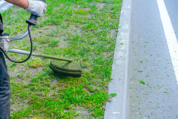 Man mows grass with a lawn mower near the road.