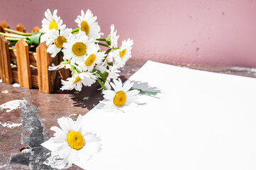 White blank sheet and a bouquet of daisies in a wooden box on a wooden background. The concept of purity, freshness