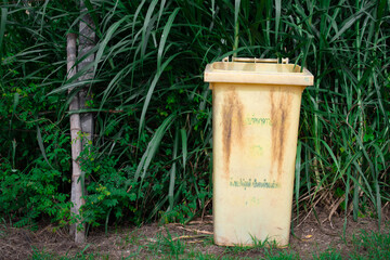 Fototapeta premium green plant graden with yellow big trash plastic bin