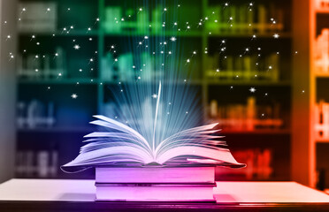 Open Book with abstract magic bright light on wooden table and blurred bookshelf in the library. © masterjew