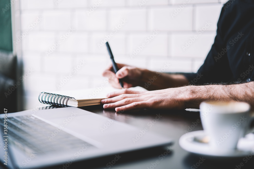 Poster cropped image of businessman dressed in black shirt writing down text information in notepad while w