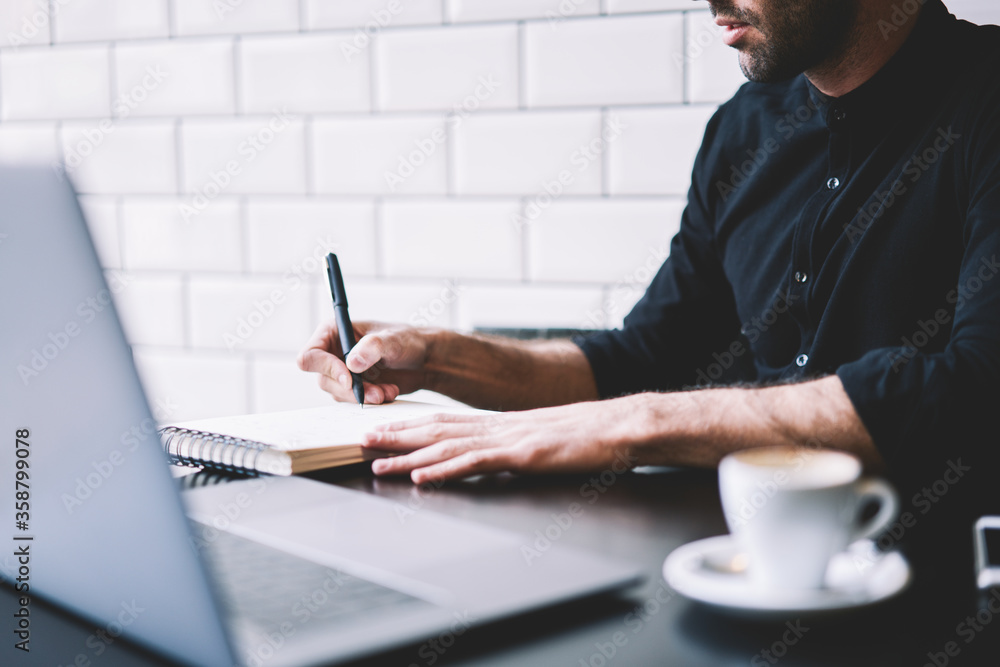 Poster cropped image of stylish businessman dressed in black shirt making notes in notepad working at moder