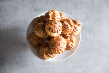 Small profiteroles on plate with cream on kitchen table closeup. Cooking at home. Top view.