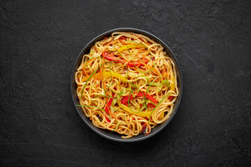 Chilli Garlic Hakka Noodles in black bowl on dark slate tabpe top. Indo-Chinese vegetarian cuisine dish. Indian veg noodles with vegetables. Classic Asian meal. Copy space. Top view