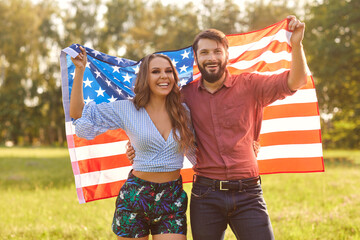 Happy couple with American flag outdoors. Young man and his girlfriend with national banner...