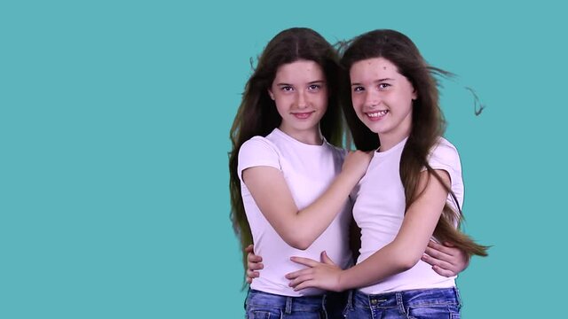 Attractive adorable cheerful pretty little sisters having their long hair wafting stand together holding each other in hugs, smile, look at the camera. Family and childhood concept.