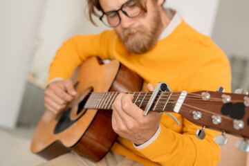 Bearded young musician with string musical instrument tuning acoustic guitar