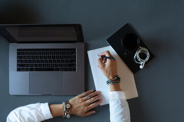 Overhead shot of a woman using different electronic devices. Overhead stock photo of a woman working on her laptop, smartphone, and notes placed on a dark surface office desk.  © Jelena Jojic Tomic