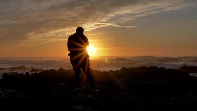 Slow motion men warrior dancer practicing silhouette tai chi karate kung Fu on the rocky stones horizon at sunset or sunrise.Silhouette on a background of dramatic epic waves at pacific coast