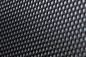 Macro shot of a black metal surface with round holes, gray background.
