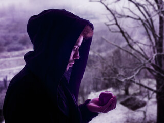 young man holding an apple in the winter landscape - mysterious guy in a black hood - cold season of the year