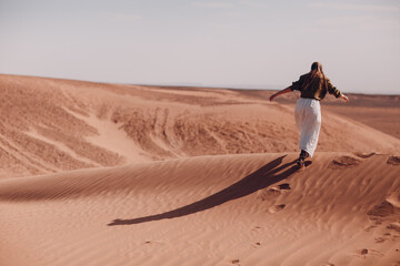 Fototapeta na wymiar Young woman runs on sand dunes in desert Sahara