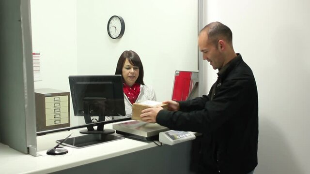 Man posting out a package / Parcel at the Post Office Counter - The Female assistant serves the man - Stock Video Clip Footage 