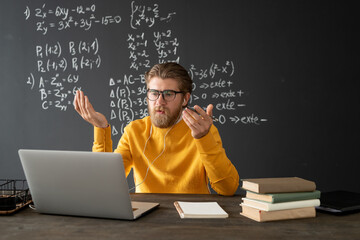 Confident teacher in eyeglasses looking at his audience on laptop display