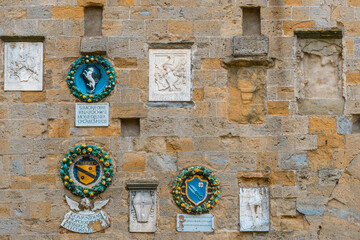 Medieval coats of arms of local noble families on a stone wall in the historic old town of Volterra, Tuscany, Italy.