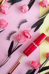 Obraz na płótnie Canvas premium makeup brushes, lipstick and false eyelashes on a colored pink and yellow background, creative cosmetics flat lay